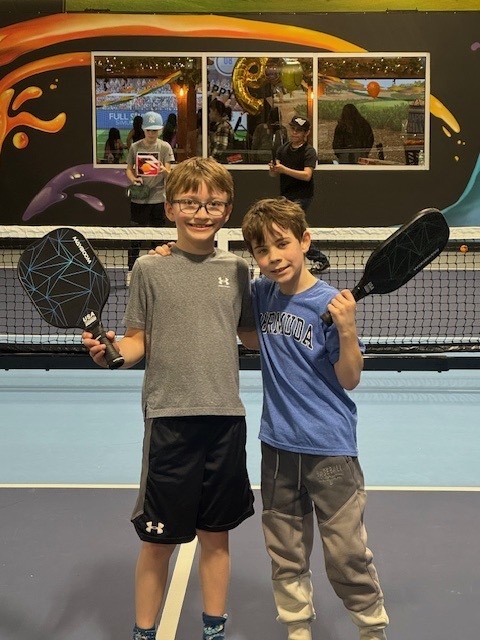 Two boys with pickleball paddles at a birthday party on the courts