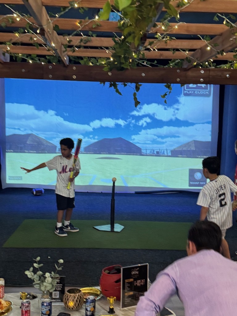 Boy hitting off a tee in the baseball simulator during a birthday party
