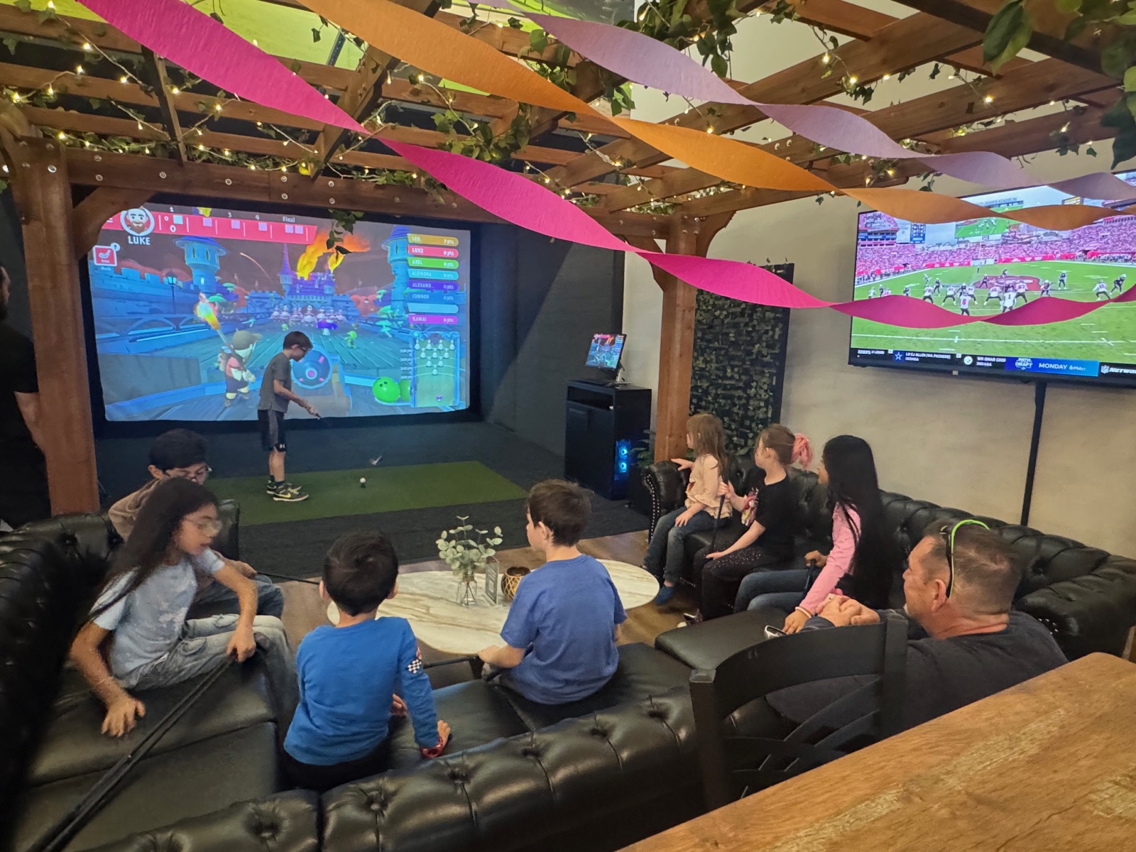 Kids watching a friend play on the golf simulator during a party